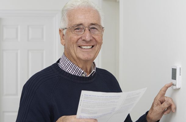 A man smiling whilst turning down his haetinga nd holding an energy bill